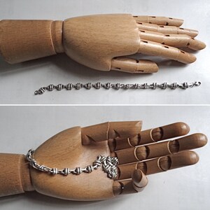 May include: A silver chain bracelet with a knotted design. The bracelet is shown on a wooden hand model.