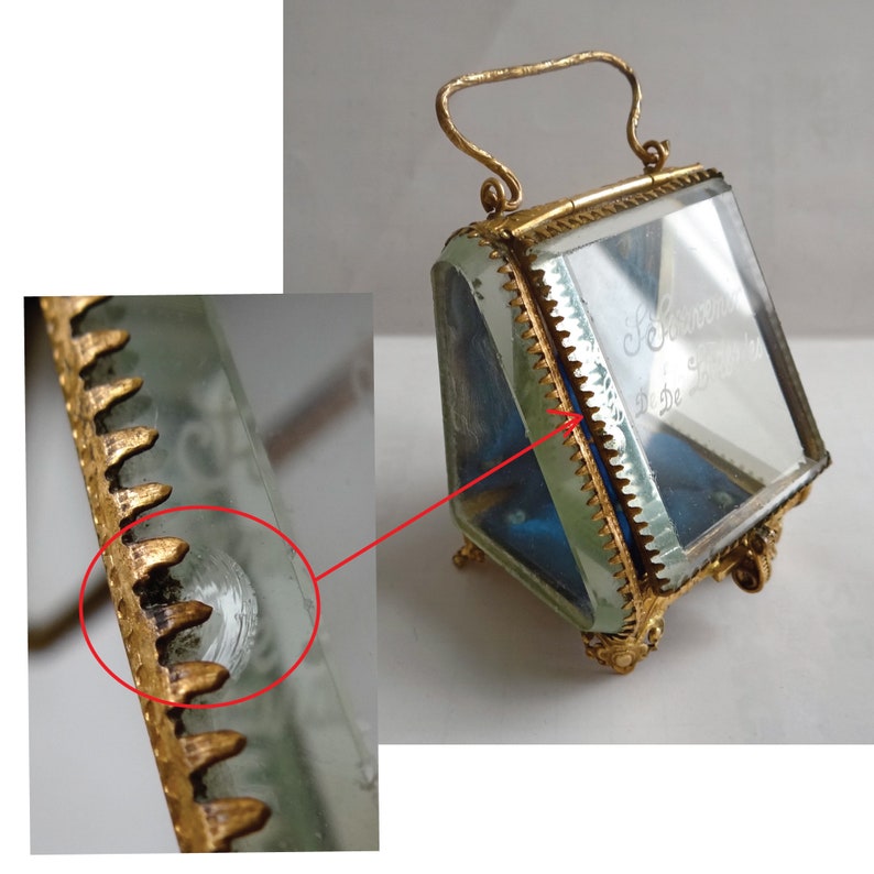 Op de afbeelding: Een kleine, transparante glazen doos met een gouden metalen frame en een handvat. De doos heeft een blauwe fluwelen voering en een inscriptie op het glas die luidt "Souvenirs de l'Exposition de 1878".