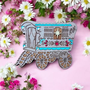 Peut inclure: Une découpe en bois d'une roulotte gitane grise et bleue avec une étoile sur le devant. La roulotte est décorée de fleurs rouges et bleues et de strass.