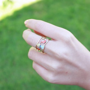 May include: A gold-toned open-work ring featuring colourful enamel details of a small figure with yellow hair, a red fox, and small stars. The band has a wavy, irregular edge design and is crafted with a cutout style that showcases the enamel motifs.