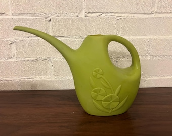 Könnte beinhalten: Eine hellgrüne Gießkanne mit langem Ausguss und gebogenem Griff. Die Gießkanne hat ein Blumendesign auf der Seite. Die Gießkanne ist aus Kunststoff und steht auf einer dunkelbraunen Holzoberfläche.