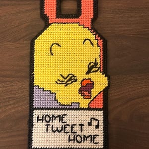 May include: A yellow bird with a pink and purple background, singing with its mouth open. The bird is on a white background with the text "Home Tweet Home" and musical notes.