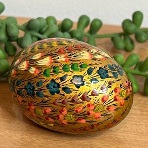 May include: A decorative, golden egg with a floral design in shades of pink, blue, and green. The egg is hand-painted with intricate details, showcasing a blend of colors and patterns. The egg is a unique decorative item.