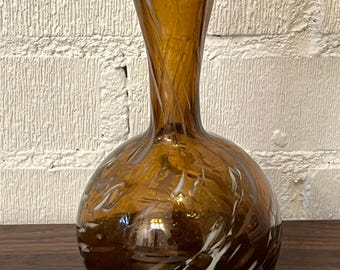 Puede incluir: Jarrón de cristal color ámbar con borde acampanado y rizado. El jarrón tiene una base bulbosa y un cuello delgado con detalles grabados. Rayas blancas giran alrededor de la base. El jarrón está sobre una superficie de madera oscura.