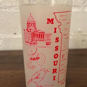May include: A clear glass with a red design featuring the state of Missouri. The design includes the state capitol building, state flower, state bird, and the word "Missouri" in large letters. The glass also lists several cities.