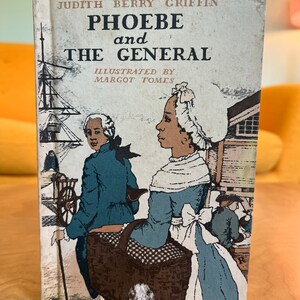 K&ouml;nnte beinhalten: Ein Vintage-Kinderbuchcover mit einer Illustration von zwei Personen, die eine Stra&szlig;e entlang gehen. Das Buch tr&auml;gt den Titel "Phoebe und der General" von Judith Berry Griffin, illustriert von Margot Tomes.