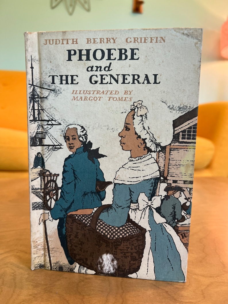 K&ouml;nnte beinhalten: Ein Vintage-Kinderbuchcover mit einer Illustration von zwei Personen, die eine Stra&szlig;e entlang gehen. Das Buch tr&auml;gt den Titel "Phoebe und der General" von Judith Berry Griffin, illustriert von Margot Tomes.