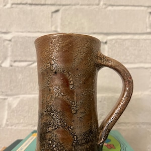 May include: A brown ceramic mug with a crackled glaze and a handle. The mug has a rustic, handmade look.