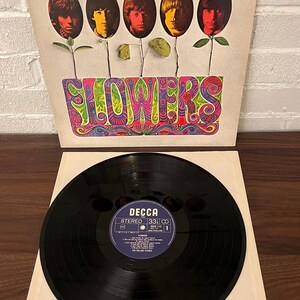May include: The Rolling Stones Flowers vinyl record album with a square cardboard sleeve featuring five oval portraits of band members above the word FLOWERS in colorful psychedelic lettering and a black vinyl disc with a Decca label.