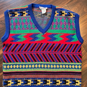 May include: A colorful knitted vest with a geometric pattern in shades of red, blue, green, yellow, and black. The vest has a V-neck and sleeveless design.