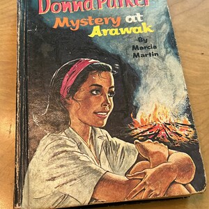 May include: A vintage paperback book titled "Donna Parker Mystery at Arawak" by Marcia Martin. The cover features a young woman with a pink headband sitting by a campfire.