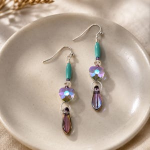 Peut inclure: Une paire de boucles d'oreilles pendantes avec des crochets argentés, des perles cylindriques turquoise, des intercalaires en cristal facetté transparent, des perles en forme de cœur violet irisé et des pendentifs en verre goutte d'eau violet foncé.
