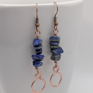 Peut inclure: Une paire de boucles d'oreilles pendantes composées de éclats de pierre lapis-lazuli bleu brut et poli, enfilés sur du fil de cuivre. Chaque boucle est suspendue à un crochet en cuivre et se termine par une petite boucle infinie en cuivre.