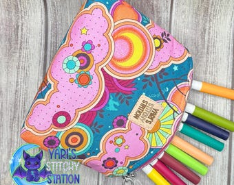 May include: A colorful, patterned pencil case with a zipper, filled with markers. The case features a vibrant design with pink, orange, and teal hues, and the text "Yari's Stitchy Station".