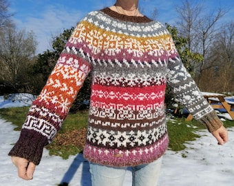Può includere: Un maglione di lana colorato con un motivo geometrico in tonalità di marrone, arancione, rosa, bianco e grigio.