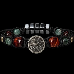 Può includere: Un braccialetto macramè nero con un elemento centrale argentato a forma di albero della vita. Il braccialetto incorpora perline di occhio di tigre rosso, verdi e argentate. Il design include un accento metallico quadrato e un cordoncino nero.