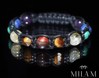 Puede incluir: Un brazalete trenzado negro con siete cuentas de piedras preciosas de colores. Las cuentas son de los colores del arcoíris, comenzando por el rojo y terminando por el morado.