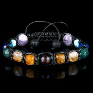 May include: A black braided bracelet with various colored gemstone beads, including amethyst, tiger's eye, and red jasper.