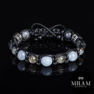 Può includere: Bracciale artigianale con design macramè e mix di pietre preziose. Presenta perline azzurre, gialle e grigie, con elementi metallici argentati. Il bracciale è esposto su sfondo nero.