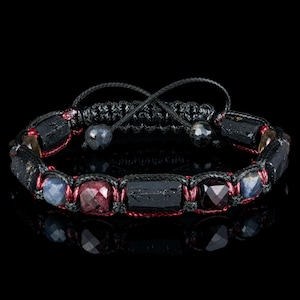 May include: A black braided bracelet with red thread and black, blue, and red gemstone beads.