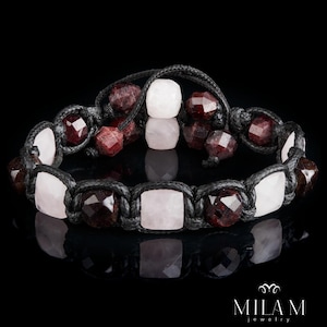 May include: A handmade bracelet featuring alternating rose quartz and garnet gemstones, strung on a black cord. The bracelet has a macrame design and is displayed against a black background. The brand name "MILAM jewelry" is visible.