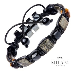 Puede incluir: Un brazalete trenzado negro con cuentas doradas, marrones y negras. El brazalete tiene un cierre de nudo deslizante y presenta un amuleto de hematites.