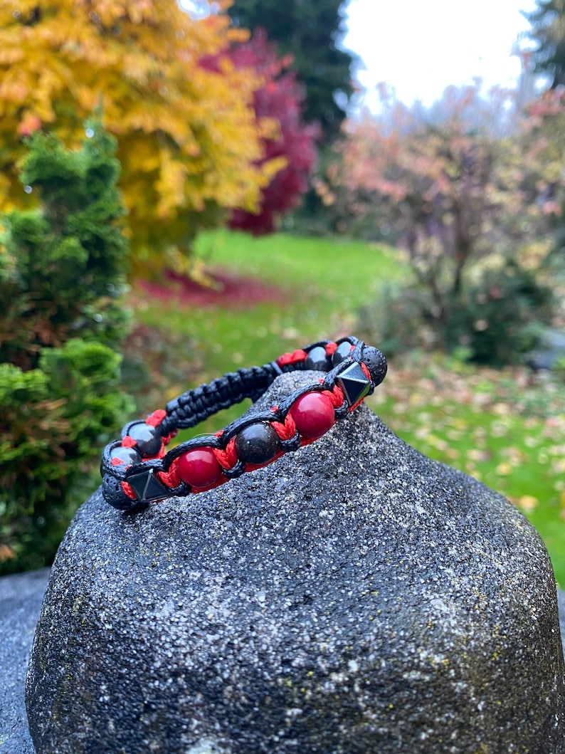 May include: A black beaded bracelet with red gemstone beads and black lava beads. The bracelet is tied with a black cord and has a knot closure.