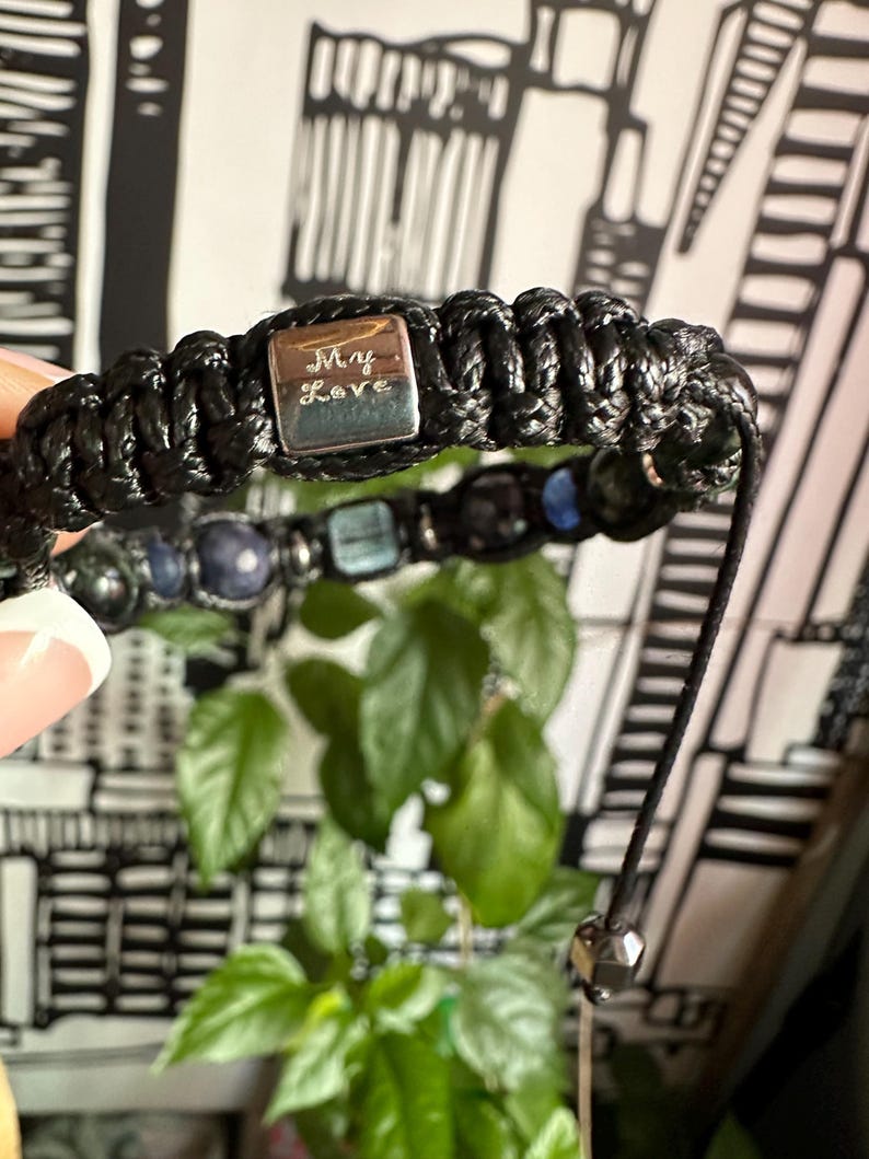 May include: Black braided bracelet with a silver charm that says "My Love". The bracelet also has blue and green gemstone beads.