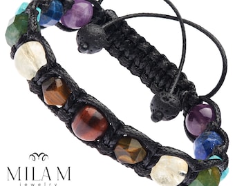 Puede incluir: Una pulsera trenzada negra con una variedad de cuentas de piedras preciosas de colores. La pulsera incluye cuentas en tonos verdes, azules, morados, amarillos y marrones. La pulsera también tiene cuentas de roca volcánica negra y cordones negros ajustables. La marca "MILAM jewelry" es visible.