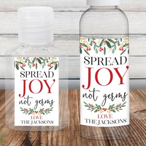May include: Two clear plastic bottles of hand sanitizer with festive Christmas labels. The labels feature a green and red wreath with gold accents and the text "Spread Joy not germs". The smaller bottle has the text "Love The Jacksons" and the larger bottle has the text "Love The Jacksons".