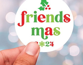 May include: A white round sticker with the text "friends mas 2024" in red and green letters. A green holly sprig with red berries is above the text.