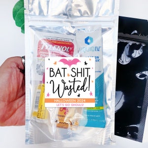 May include: A clear plastic bag filled with various items, including packets of Tylenol, Liquid I.V., and a cinnamon candy. A sticker with the text "BAT SHIT, Wasted! HALLOWEEN 2024 LET'S GO GHOULS!" is centered on the bag.