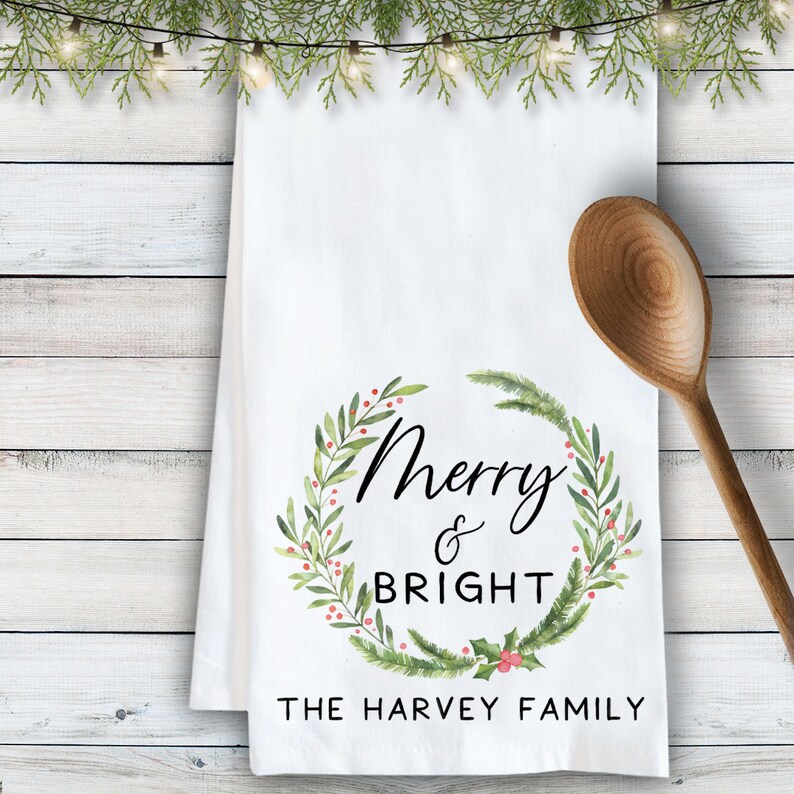 May include: White kitchen towel with a green and red watercolor wreath that says "Merry & Bright" and "The Harvey Family".