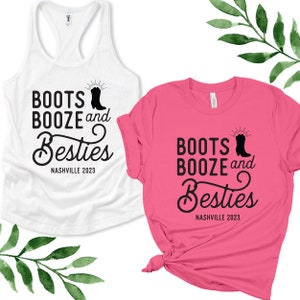May include: Two t-shirts with a black graphic design that says "Boots Booze and Besties Nashville 2023". One t-shirt is white and the other is pink.