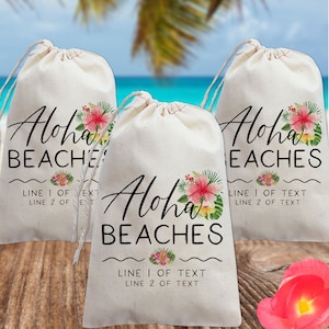 May include: Three white cotton drawstring bags with the text "Aloha Beaches" printed in black. Each bag has a floral design with pink and yellow flowers and green leaves. The text "Line 1 of Text" and "Line 2 of Text" is printed below the floral design.