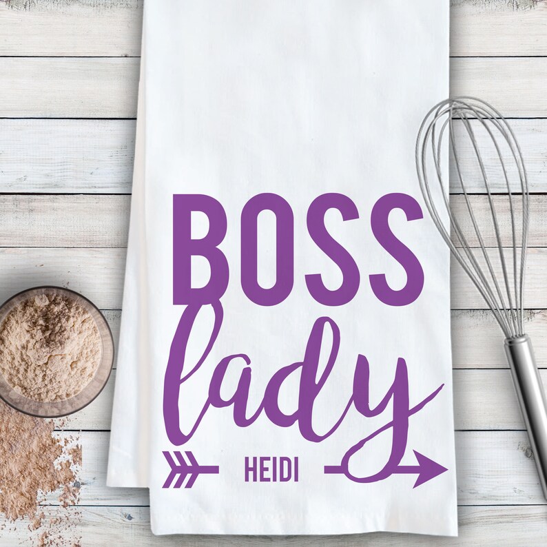 May include: White kitchen towel with purple text that reads "BOSS lady" with an arrow pointing to the right and the name "HEIDI" written below the arrow.