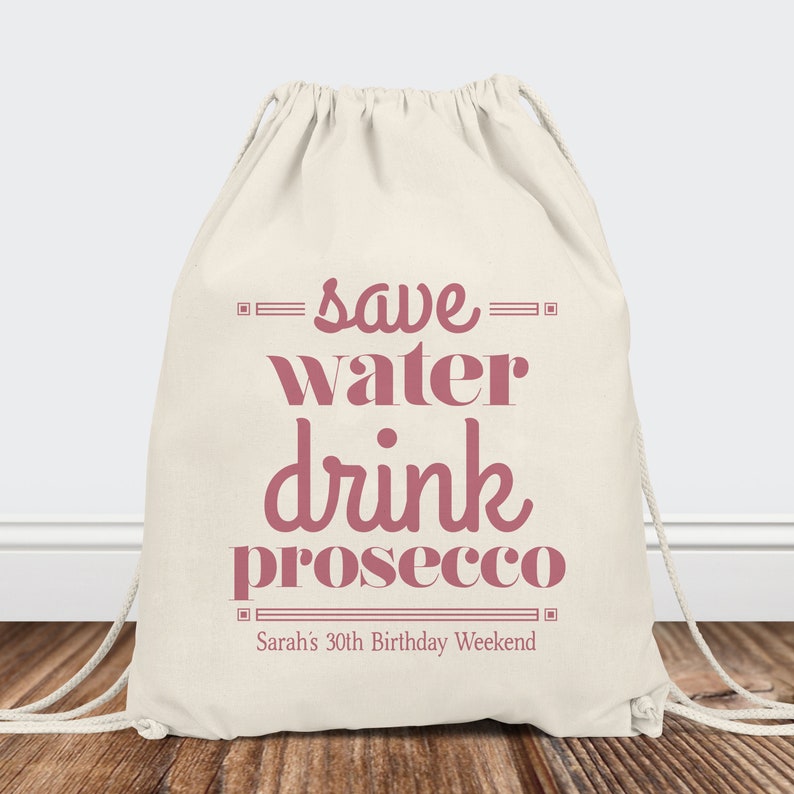 May include: A white drawstring bag with the text "save water drink prosecco" in pink. The bag also has the text "Sarah's 30th Birthday Weekend" in pink.