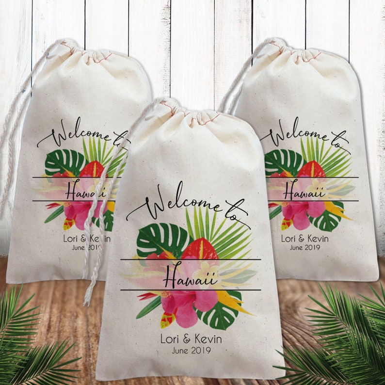 May include: Three white cotton drawstring bags with a tropical floral design and the text "Welcome to Hawaii" and "Lori & Kevin June 2019".
