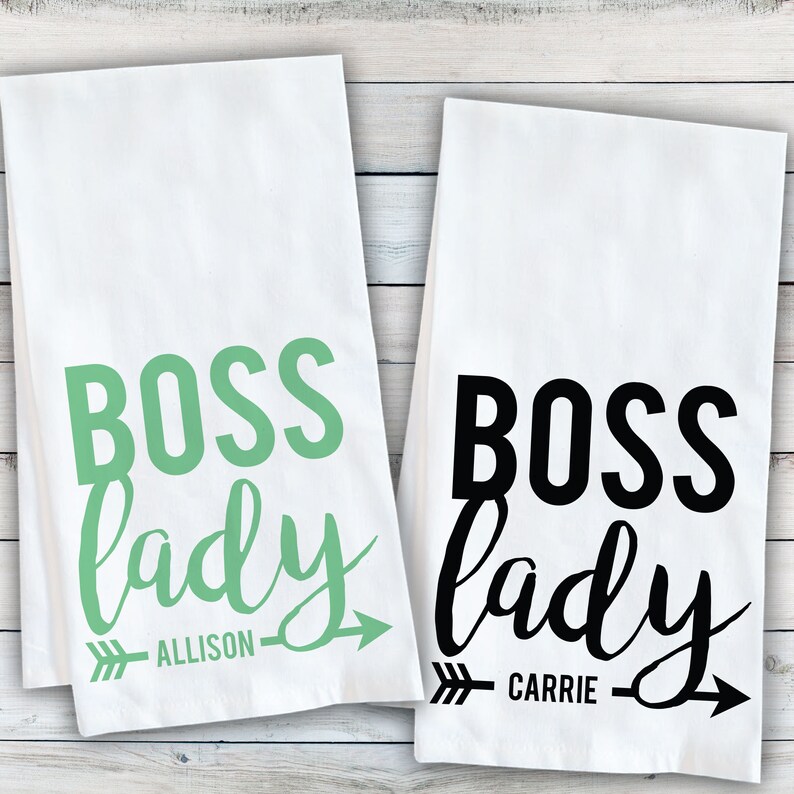 May include: Two white kitchen towels with the text "Boss lady" in black and green lettering. The towels have an arrow with the names "Allison" and "Carrie" written below.