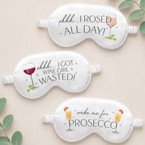 May include: Three white satin sleep masks with elastic bands. Each mask has a different wine-themed graphic and text: "shhh... I ROSED ALL DAY!", "shhh... I GOT WINE GIRL WASTED!", and "wake me for PROSECCO".