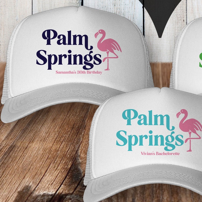 May include: Two white trucker hats with a pink flamingo and the text "Palm Springs" in blue and teal. The first hat says "Samantha's 30th Birthday" and the second hat says "Vivian's Bachelorette".