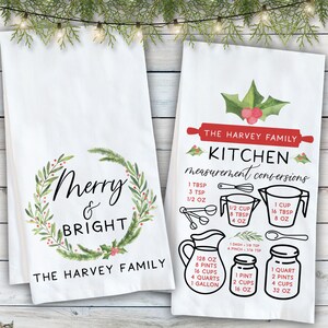 May include: Two white kitchen towels with a Christmas theme. One towel features a green wreath with the text "Merry & Bright" and "The Harvey Family". The other towel has a red and green holly design and the text "The Harvey Family Kitchen measurement conversions" with a list of common kitchen measurements.