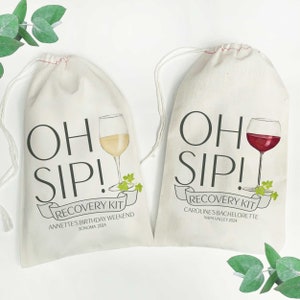 May include: Two white cotton drawstring bags with the text "OH SIP! RECOVERY KIT" printed on them. The bag on the left has a glass of white wine and the text "ANNETTE'S BIRTHDAY WEEKEND SONOMA 2024". The bag on the right has a glass of red wine and the text "CAROLINE'S BACHELORETTE NAPA VALLEY 2024".