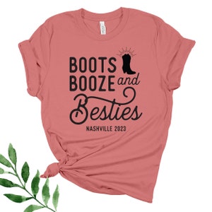 May include: A pink t-shirt with the text "Boots Booze and Besties Nashville 2023" and a black silhouette of a cowboy boot.