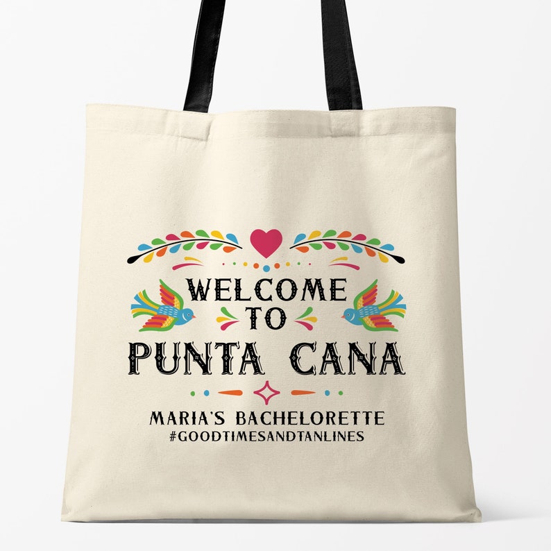 May include: A white canvas tote bag with black handles. The bag has a colorful design with the text "Welcome to Punta Cana" and the words "Maria's Bachelorette #GoodTimesAndTanLines".