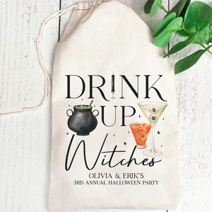 May include: White cotton drawstring bag with the text "Drink Up Witches" in black. The bag also features a black cauldron with green liquid, a martini glass with an eyeball, and a red cocktail glass. The text "Olivia & Erik's 3rd Annual Halloween Party" is also printed on the bag.