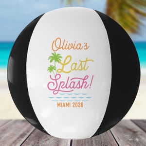 May include: A black, white, and colorful beach ball with the text "Olivia's Last Splash!" in orange, yellow, and pink. The ball also features palm trees and the text "Miami 2026".
