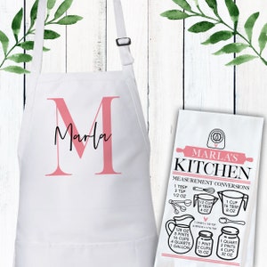 May include: White apron with a pink letter M and the name Marla printed on it. A white kitchen towel with the text "Marla's Kitchen" and measurement conversions in black and white.