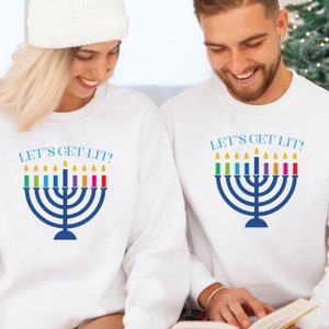 May include: Two white sweatshirts with the text "Let's Get Lit!" and a menorah with rainbow candles.