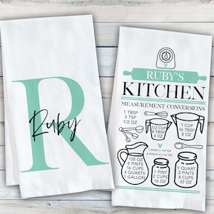 May include: Two white kitchen towels. One features a large mint green letter R with the name Ruby in black script. The other displays a mint green rolling pin icon, the text Ruby's Kitchen, and a black graphic chart of measurement conversions.